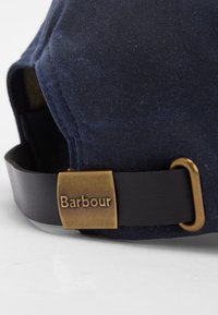 Boné azul marinho com um tecido texturizado, apresentando uma tira de couro preto e uma fivela de bronze com o texto "Barbour" embutido.