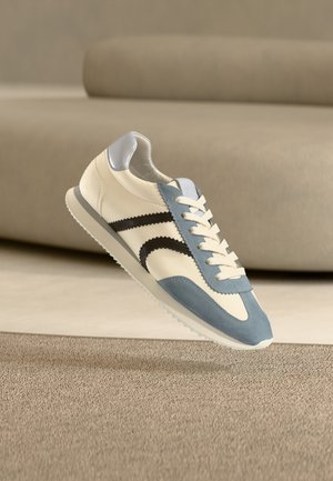 Cremefarbener und blauer Sportschuh mit einer strukturierten Oberseite, zwei schwarzen Streifen und einer Schnürung vorne. Verfügt über eine weiße Gummisohle und einen gepolsterten Kragen.