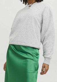 Felpa grigia con vestibilità ampia, maniche lunghe e polsini a coste, abbinata a una gonna midi in satin verde lucido con cucitura laterale.