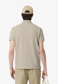 Beige polo t-shirt med korta ärmar, texturerad tyg och rak fåll. Kombinerad med matchande beiga byxor och en ljus kaki keps.