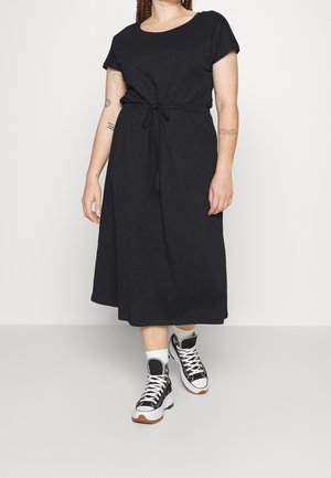 Zwarte, knie-lange jurk met korte mouwen, taille met koordje en een losse pasvorm, gecombineerd met zwart-witte sneakers en witte sokken.