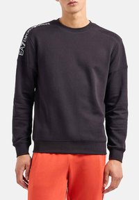 Felpa nera realizzata in tessuto morbido, con collo rotondo e maniche lunghe. Logo "EA7" stampato sulla spalla sinistra. Polsini e orlo a coste.