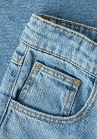 Close-up of light blue denim jeans pocket with visible stitching and textured fabric details.