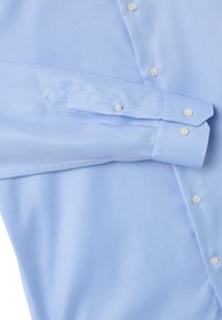 Camicia a maniche lunghe di colore azzurro chiaro con polsini con bottone e bottoni bianchi, esposta distesa su uno sfondo bianco.