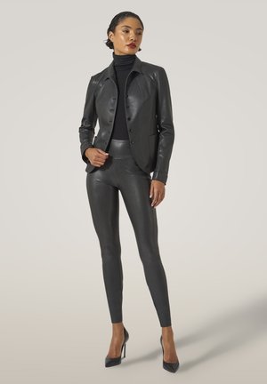 Zwarte leren jas met een aansluitende silhouet, gecombineerd met hoge taille, gestructureerde zwarte leggings en hoge hakken.