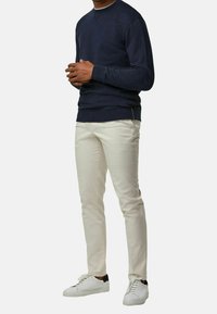 Marinblå sweatshirt med rundad hals och långa ärmar, i kombination med krämfärgade slim-fit byxor och vita sneakers med svarta detaljer.