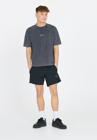 Harmaa puuvillapaita rento malli, yhdistettynä mustiin shortseihin. Paidassa on minimalistinen logo ja klassiset mustat tennisasuket.