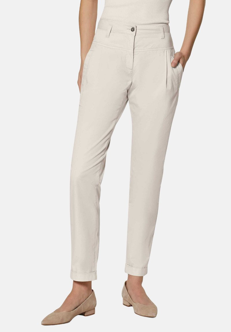 Lichtbeige broek met een taps toelopend been, voorplooien en zijzakken. Gemaakt van een soepele, lichte stof. Opgerolde mouwdetails.