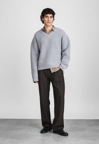 Γκρι πλεκτό πουλόβερ με σχέδιο V, με άνετη εφαρμογή και ραβδωτή υφή, συνδυασμένο με μπεζ πουκάμισο με κουμπιά και σκούρους παντελόνες.