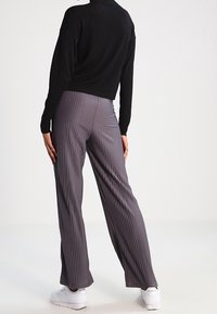 Pantaloni larghi grigi a pieghe, in tessuto morbido, con vita alta e una caduta elegante. Abbinati a un top nero a maniche lunghe e sneakers bianche.