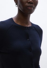 Tmavomodrý pletený sveter s okrúhlym výstrihom, raglánovými rukávmi a šiestimi gombíkmi vpredu. Mäkká textura a priliehavý strih.