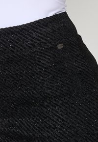 Zwarte gestreepte rok met een golvend patroon, accenten van metallic draad en een klein metalen logo detail bij de tailleband.