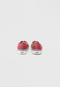 Červené kárované slip-on topánky s bielymi gumovými podrážkami a akcentmi. Z pohľadu zozadu je vidieť hladký povrch a výrazné logo na päte.