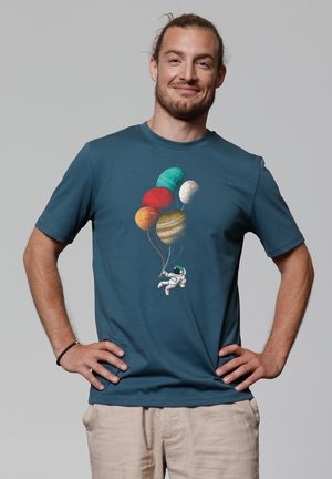 Teal short-sleeve t-shirt featuring an astronaut holding colorful planet balloons. Soft fabric with a round neckline and relaxed fit.