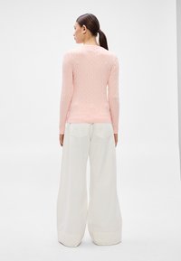 Svetloružový sveter s dlhými rukávmi a vzorom káblového pletenia, skombinovaný s bielymi širokými nohavicami s dvomi zadnými vreckami. Jednoduchý dizajn so štruktúrou.