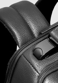 Primer plano de mochila de cuero negro, con superficie texturizada, correas acolchadas, cremallera suave y detalles metálicos brillantes.