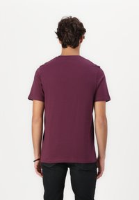 T-shirt à manches courtes en coton bordeaux profond, avec un col rond classique et une texture lisse. Design simple sans motifs ni accents.