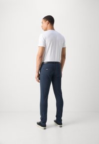 Calças azul-marinho com um corte justo, apresentando uma textura suave e bolsos traseiros. Combinadas com uma t-shirt branca lisa e ténis pretos.