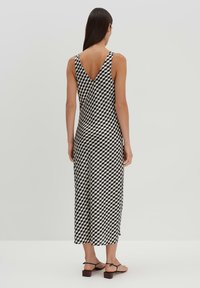 Schwarz-weiß gemustertes ärmelloses Kleid mit V-Ausschnitt, das bis zur Mitte der Waden reicht. Es zeichnet sich durch ein geometrisches Design aus und besteht aus einem glatten, leichten Stoff.