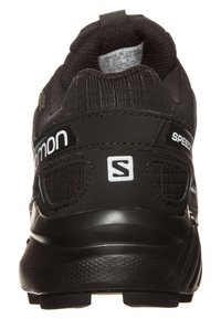 Zapatilla deportiva negra con tejido de malla texturizada, cuello acolchado y suela de goma. Presenta un logo y acentos reflectantes en el talón.