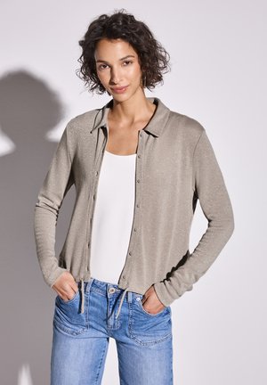 Lichtgrijze cardigan met een subtiele glans, knoopsluiting aan de voorkant, lange mouwen en een relaxte pasvorm, gecombineerd met een witte tanktop en blauwe spijkerbroek.