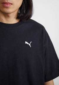 Tricou din bumbac negru cu mâneci scurte, având un logo alb Puma pe pieptul stâng. Design simplu, croială normală și textură netedă.