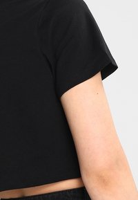 Maglietta nera cropped con maniche corte, realizzata in morbido cotone. Presenta un design semplice, una texture liscia e nessun abbellimento visibile.