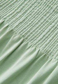 Tissu vert clair avec un détail de smocks texturés en haut et de doux plis fluides en dessous. Surface lisse et matière extensible.