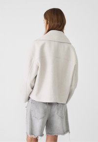 Light grey cropped jacket with a large collar, made from soft fabric. Paired with frayed-edge gray denim shorts.