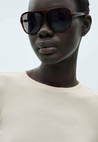 Schildpatt-Übergrößen-Sonnenbrille mit dunklen Gläsern. Das Modell trägt ein hellbeiges, geripptes Oberteil mit einem klassischen runden Ausschnitt.