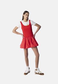Rode skaterjurk met verstelbare bandjes en een geplooide taille, gecombineerd met een wit T-shirt en hoge sneakers in bruin en wit.