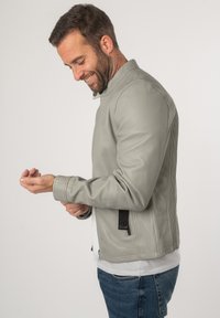 Lichtgrijze leren jas met een gladde textuur, voorzien van een staande kraag en een zijrits, gestyled met geribbelde details op de mouwen.