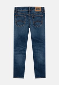 Lieknos džinsinės kelnės tamsiai mėlynos spalvos, su oranžiniais siūlais. Turi dvi galines kišenes ir odinį ženklelį su užrašu "TOMMY HILFIGER" ant juosmens.