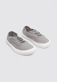 Scarpe in tela grigia con suole in gomma bianca, dotate di lacci decorativi grigi e un design semplice. Texture liscia e punta larga.