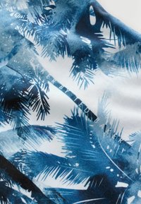 Tissu blanc avec des motifs de feuilles tropicales bleues. Présente différentes nuances de bleu, une texture lisse et un détail de marque subtil dans le design.