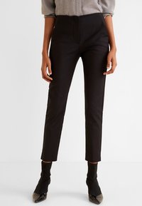 Pantaloni neri su misura realizzati in tessuto liscio, caratterizzati da una silhouette aderente, vita medio-alta e lunghezza cropped, abbinati a tacchi neri.