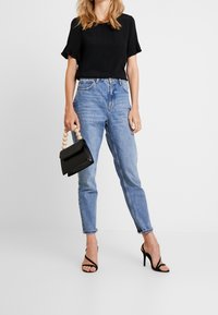 Svart kortärmad topp i kombination med högmidjade ljusblå raka jeans. Accessoarer inkluderar en svart handväska med pärlhandtag och svarta klackar.