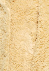 Texturerad beige tyg med en fluffig, mjuk känsla. Har ett vågigt mönster och tät lugg, som påminner om fårskinn eller konstpäls.