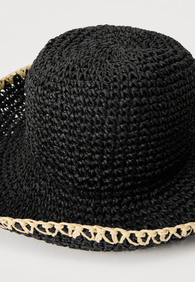 Μαύρο πλεκτό καπέλο ηλίου με φαρδύ γείσο και μπεζ πλεγμένη διακόσμηση κατά μήκος της άκρης, παρουσιάζεται πάνω σε απλό φόντο.