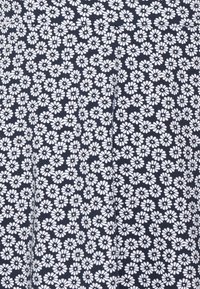 Námořnická tkanina s bílým květinovým potiskem, zahrnující malé sedmikrásky, uspořádané hustě po celé ploše, což vytváří texturovaný vzhled.