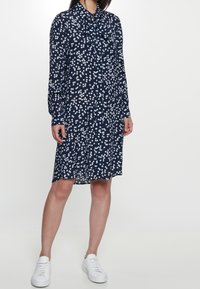 Abito della marina con pois bianchi, maniche lunghe, chiusura con bottoni e colletto a farfalla. Indossato con sneaker bianche, taglio a media lunghezza.
