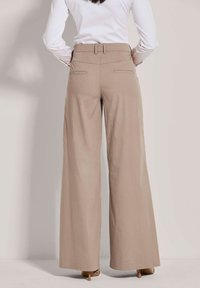Beige wijde broek met een hoge taille, gladde textuur en achterzakken. De stof lijkt licht en ademend.