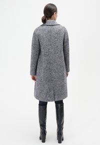 Grauer Herringbone-Wollmantel mit Reverskragen, geradem Schnitt, langen Ärmeln und Seitentaschen, kombiniert mit schwarzen kniehohen Stiefeln.