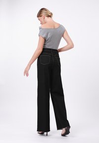 Grauer schulterfreier Oberteil mit kurzen Ärmeln, kombiniert mit hochtaillierten schwarzen Jeans. Die Jeans haben einen geraden Schnitt und sichtbare Gesäßtaschen.