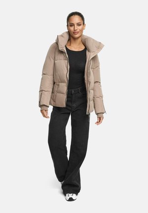 Beige pufferjack zo met een hoge kraag, lange mouwen en een ritssluiting. Gecombineerd met zwarte wijde broek en witte sneakers.