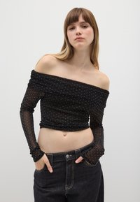 Top nero senza spalle realizzato in materiale trasparente con finitura testurizzata, caratterizzato da dettagli a pois argento e maniche lunghe aderenti.