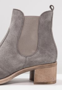 Botín de ante gris con paneles elásticos en los laterales, punta redondeada y tacón medio de bloque de madera. Acabado texturizado con detalles de costura visibles.