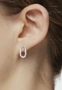 Orecchino ad anello ovale in argento con una finitura liscia e lucida. Progettato con un'apertura per facilitarne l'indossamento, mostrato su un lobo dell'orecchio.