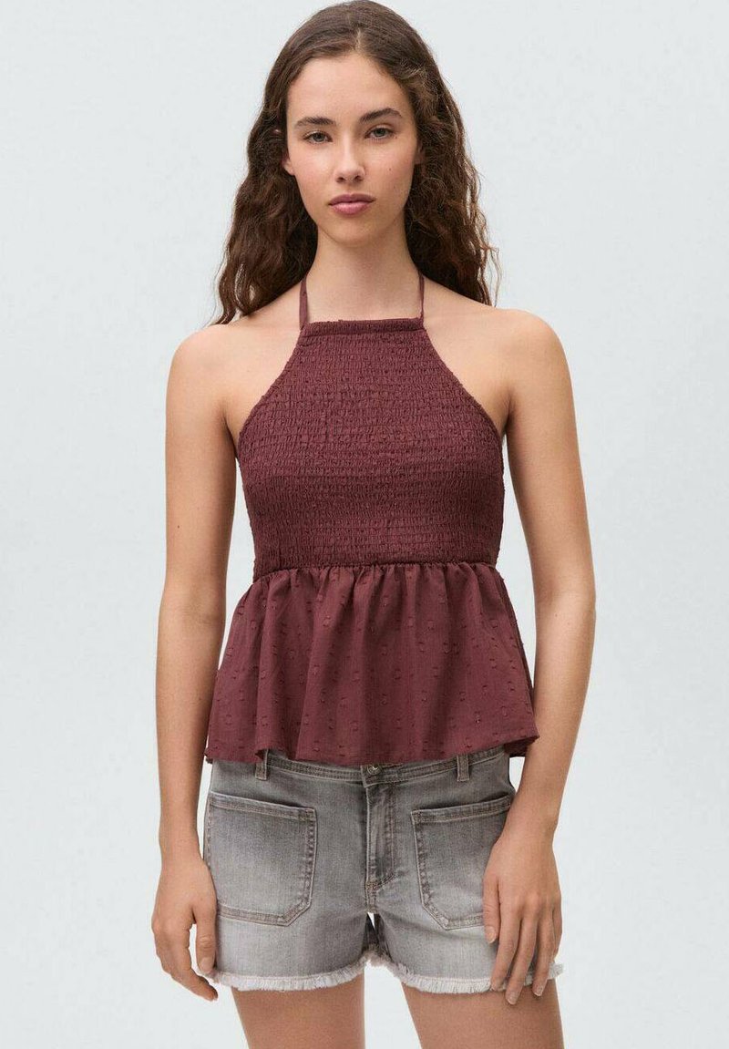 Bordo halterski top z nabrano bodice in razširjenim robom, izdelan iz teksturirane tkanine, v kombinaciji s sivimi denim kratkimi hlačami z raztrganimi robovi.