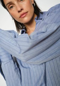 Világoskék csíkos ing, szövetből készült, gallérral és gombos elülső résszel. Hosszú ujjú, varrt mandzsettákkal. Puha tapintású.